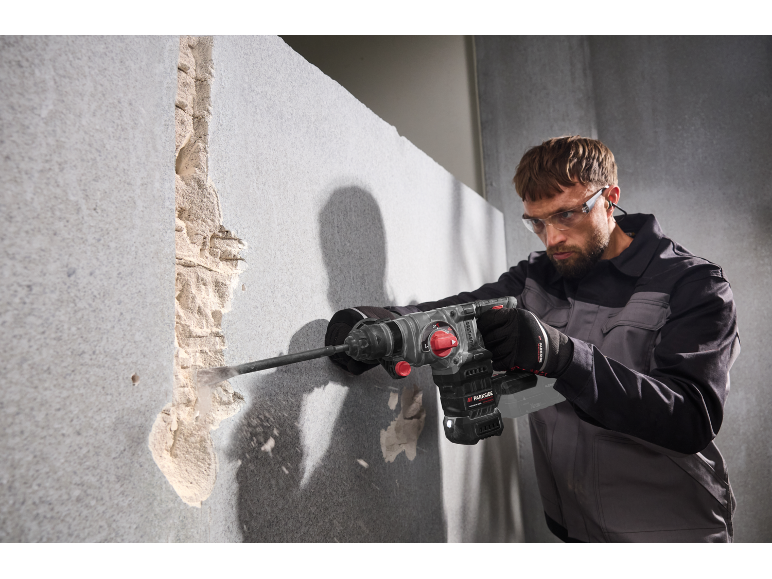 Homme avec des lunettes de sécurité utilisant un marteau perforateur pour casser un mur.