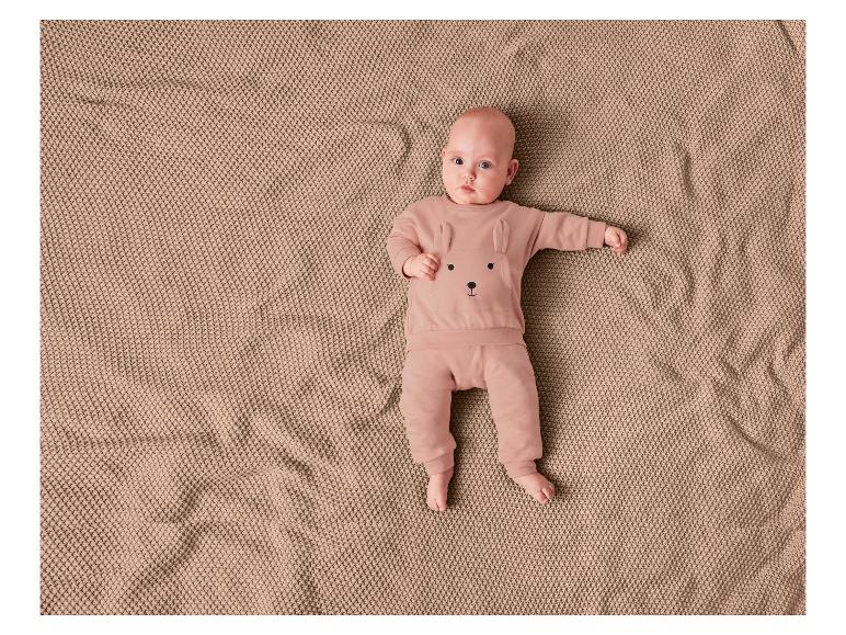 Un bébé allongé sur une couverture en tricot dans une combinaison rose avec un imprimé ours.