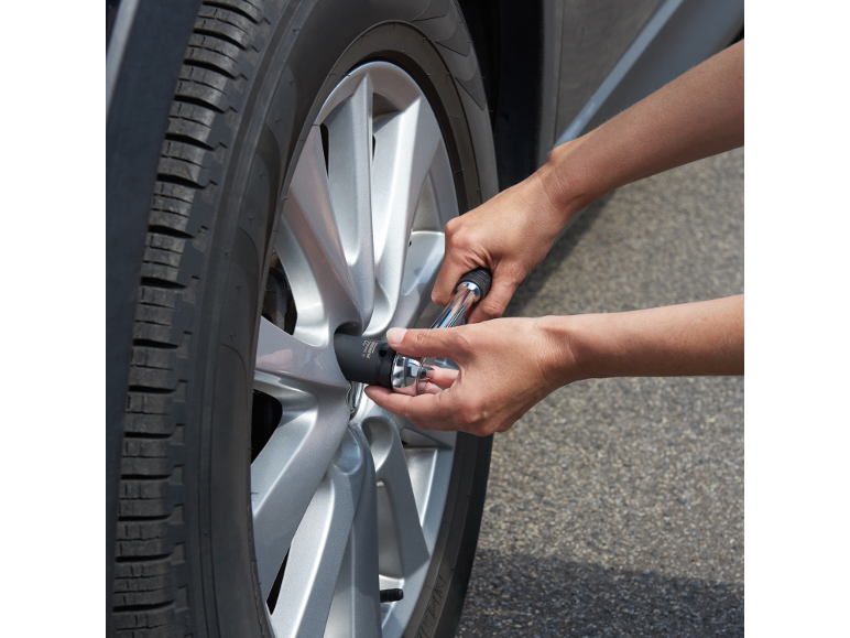Mains utilisant une clé en croix pour serrer un écrou de roue de voiture.
