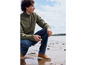 Un homme portant un sweat-shirt vert, un jean bleu et des bottes Timberland brunes.