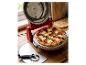 Une pizza pepperoni fraîchement cuite dans un four à pizza électrique rouge, avec une roulette à pizza à côté.
