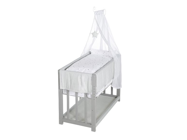 Lit bébé en bois gris avec un baldaquin blanc et une literie étoilée.