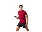 Un homme en t-shirt rouge et short noir fait de l'exercice avec des haltères.