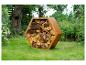 Support à bûches hexagonal en métal corten, rempli de bois, sur une pelouse.