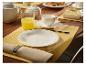 Table de petit-déjeuner avec assiettes blanches, tasses, pot, verre de jus et serviettes.