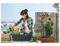 Une femme plante des fleurs dans un pot noir sur un balcon.