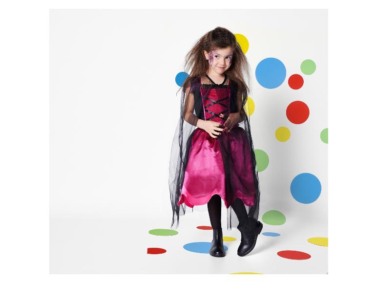 Une fille en robe rose et noire avec une cape pose devant un fond à pois colorés.