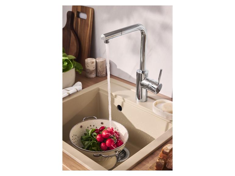 Robinet de cuisine chromé avec de l'eau coulant dans un évier beige, lavant des radis dans une passoire.