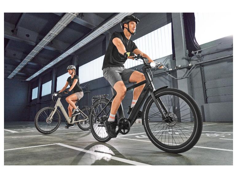Deux cyclistes sur vélos électriques, casques et vêtements de sport dans un parking.