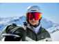 Skieuse avec casque et lunettes de ski, skis sur l'épaule, devant un panorama montagneux