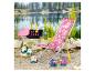 Une chaise longue rose à motifs, un panier et des canards jouets au bord d'un lac.