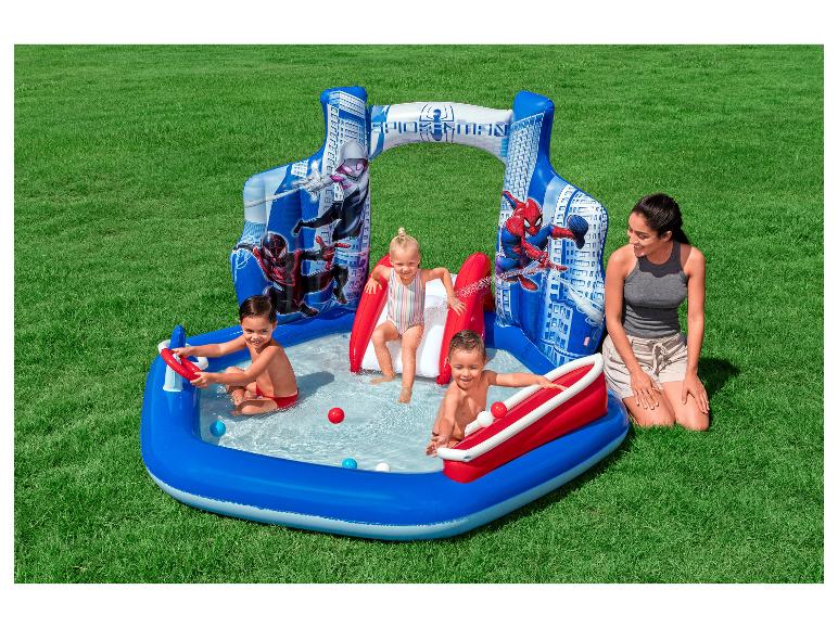 Piscine gonflable de super-héros avec toboggan, trois enfants qui jouent et une femme.