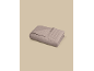 Couverture matelassée marron clair pliée avec de petits points brodés sur fond beige.