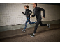 Homme et femme courant en tenue de sport noire et baskets.