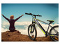 Une femme est assise sur une colline avec vue sur les nuages, à côté d'un vélo Sachs.