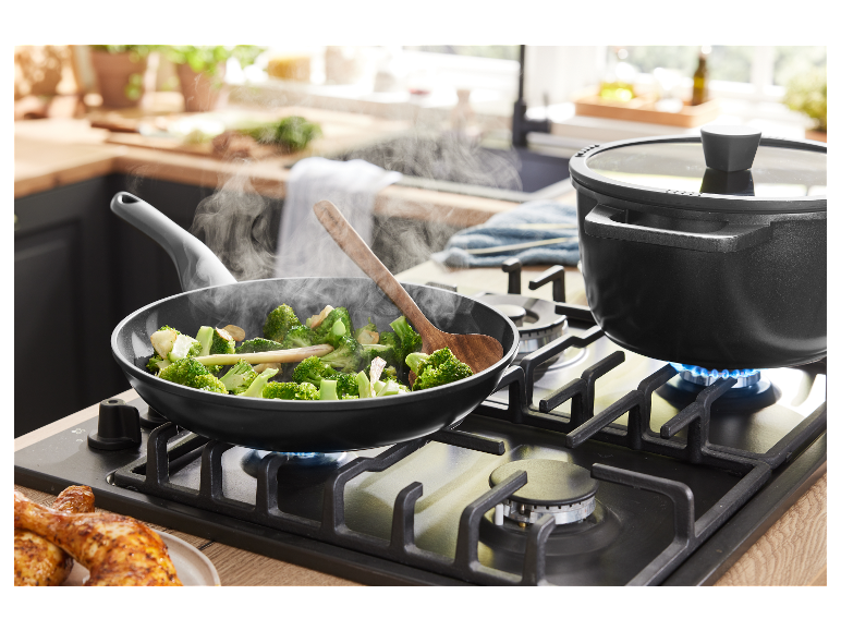 Des brocolis sont sautés dans une poêle et un plat mijote dans une casserole sur une cuisinière à gaz.