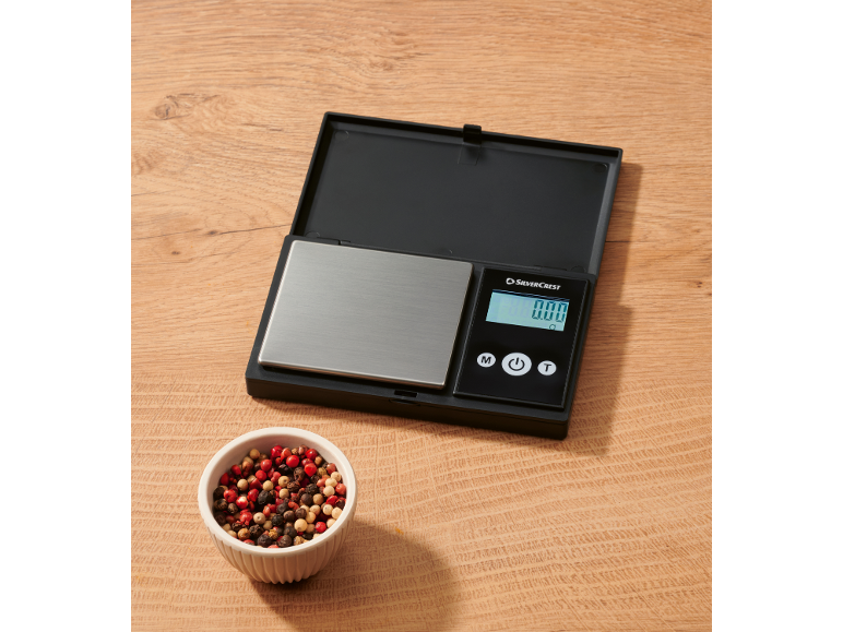 Balance numérique avec un bol de grains de poivre sur une table en bois.