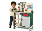 Enfant souriant jouant avec un établi de jeu vert et beige avec des outils.