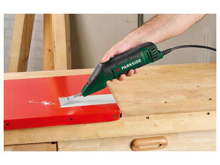 Un homme enlève de la peinture d'une surface rouge avec une ponceuse oscillante sur une table en bois.
