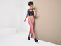 Une femme portant un soutien-gorge de sport noir et un legging rose se tient devant un mur beige.