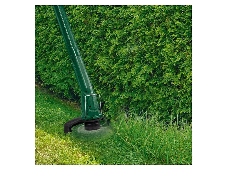 Coupe-bordure en action, taillant l'herbe haute près d'une haie.