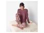 Femme en pyjama bordeaux et pantalon à motifs assise sur un pouf clair.
