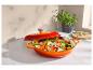 Cocotte orange avec couvercle, remplie de légumes coupés, sur un comptoir.
