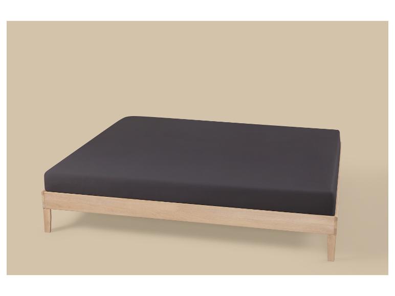 Cadre de lit en bois avec matelas gris foncé sur fond beige.