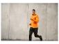 Un homme porte une veste de sport orange et un pantalon noir en courant.