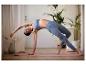 Une femme en brassière de sport bleue et leggings fait du yoga sur un tapis rose.