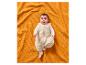 Bébé dans une gigoteuse sur une couverture gaufrée orange.