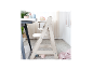 Chaise haute en bois avec vaisselle pour bébé sur une table dans une pièce lumineuse.
