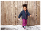 Une fille porte une veste d'hiver bleue et un pantalon rose, avec de la neige en arrière-plan.