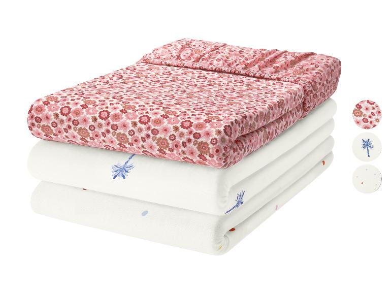 Parure de lit bébé rose fleurie et deux draps blancs avec motifs palmier et pois.