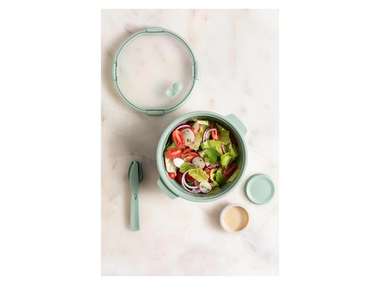 Une salade de tomates, radis et laitue dans une boîte à lunch verte avec une vinaigrette.