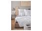 Couette et oreillers blancs sur un lit beige dans une chambre avec parquet.