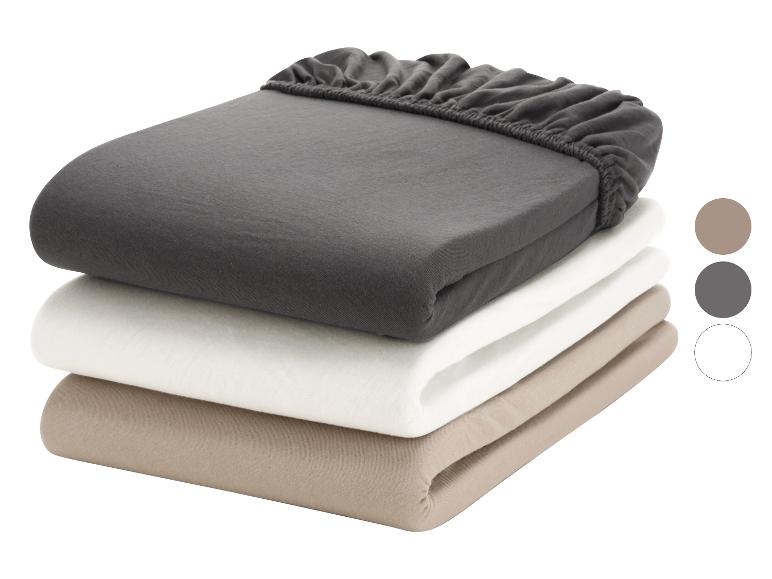 Trois draps-housses pliés, un gris foncé, un blanc et un beige, avec un élastique.