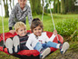 Deux enfants sur une balançoire rouge dans le jardin.