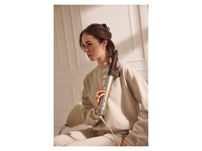 Femme tenant une brosse soufflante Cien enroulée dans ses cheveux, vêtue d'un survêtement beige.