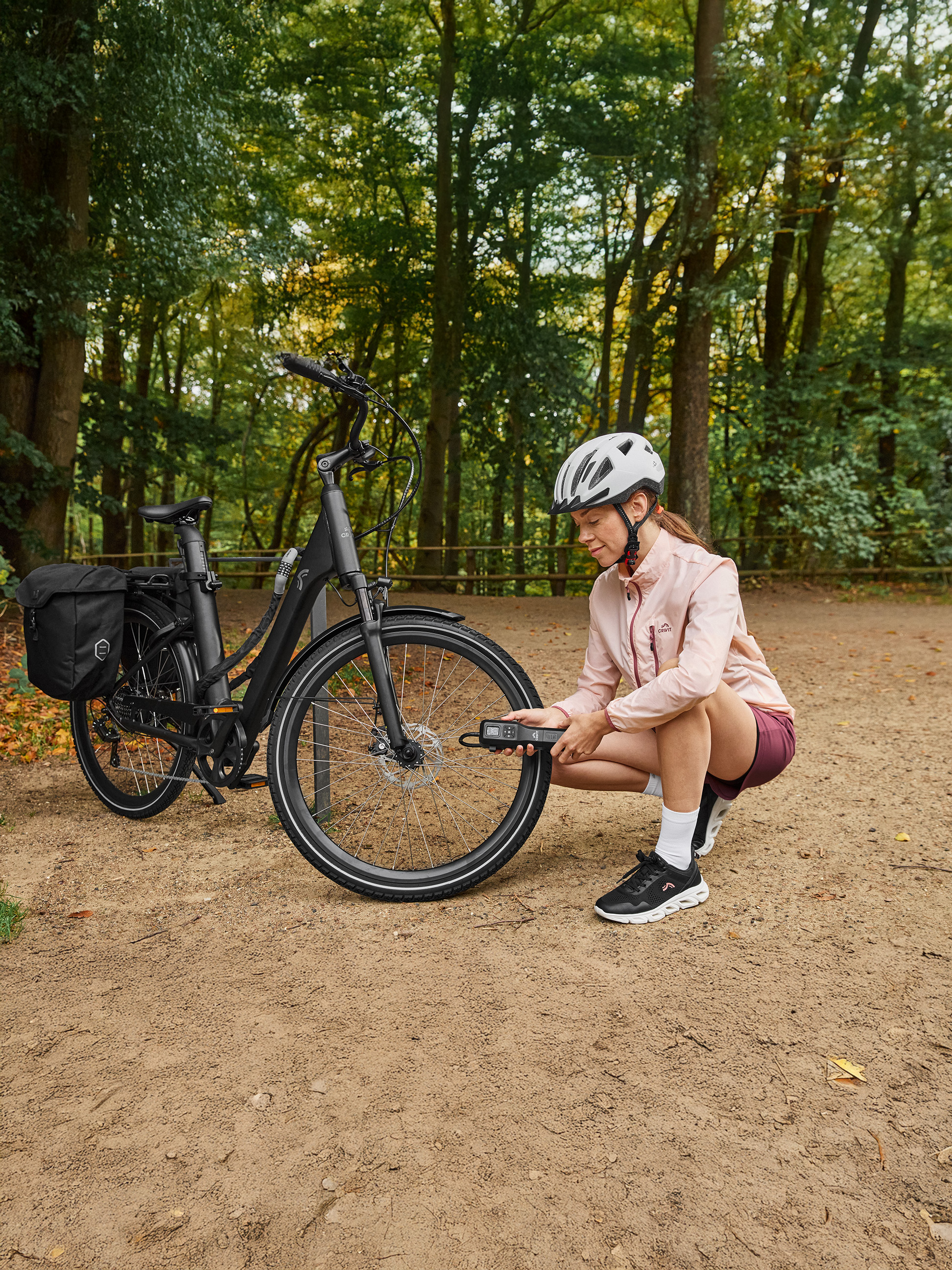 Femme en tenue de sport Crivit vérifiant la pression des pneus de son vélo électrique avec une pompe portable en forêt.