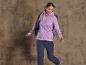 Une femme porte une veste en polaire violette à capuche et un pantalon de randonnée bleu.