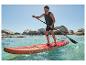 Homme sur une planche de SUP rouge pagayant en mer, avec des rochers en arrière-plan.