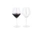 Deux verres à vin, l'un rempli de vin rouge et l'autre vide, sur fond blanc.