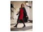 Une femme porte une robe rouge, un manteau noir et des bottes noires.