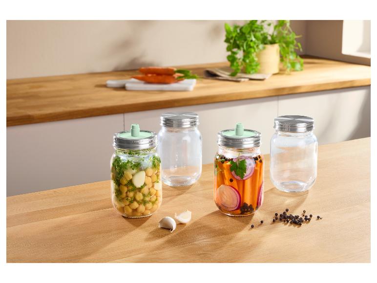 Bocaux en verre avec couvercles métalliques et valves de fermentation, avec pois chiches et carottes marinées.