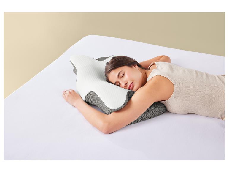 Une femme dort sur un oreiller orthopédique sur un lit blanc.