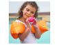 Fille souriante avec des brassards de natation orange et un jouet Baby Shark rose