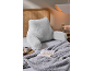 Coussin de lecture gris clair avec accoudoirs sur un lit avec un plaid et un livre.