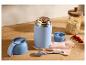 Thermos alimentaire bleu avec granola, cuillère et avoine sur une surface en bois.