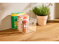 Organisateur transparent avec pâtes, épices et boîte, à côté d'une plante aromatique en pot.